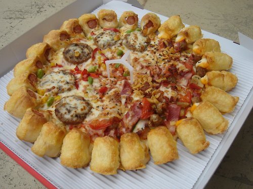 Mega Pizza A pizza with a hot dog wrapped in bacon pigs in a blanket crust. The center is filled with italian sausage, ham, bacon, bacon bits, sliced tomato, mushroom, onion, peppers, garlic chips, basil, black pepper and tomato sauce. It can also be flavored with maple syrup and ketchup. (via rinkya)